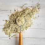 Hemp seeds with a wooden-handled spoon on a light wooden surface