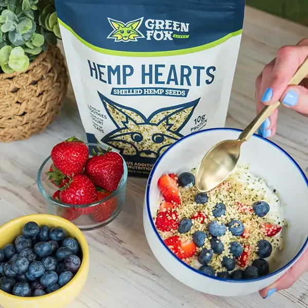 Bowl of cereal with berries, a bag of Green Fox Hemp Hearts, and a hand holding a spoon.