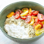 Green bowl with hummus, cherry tomatoes, and sesame seeds on a white background